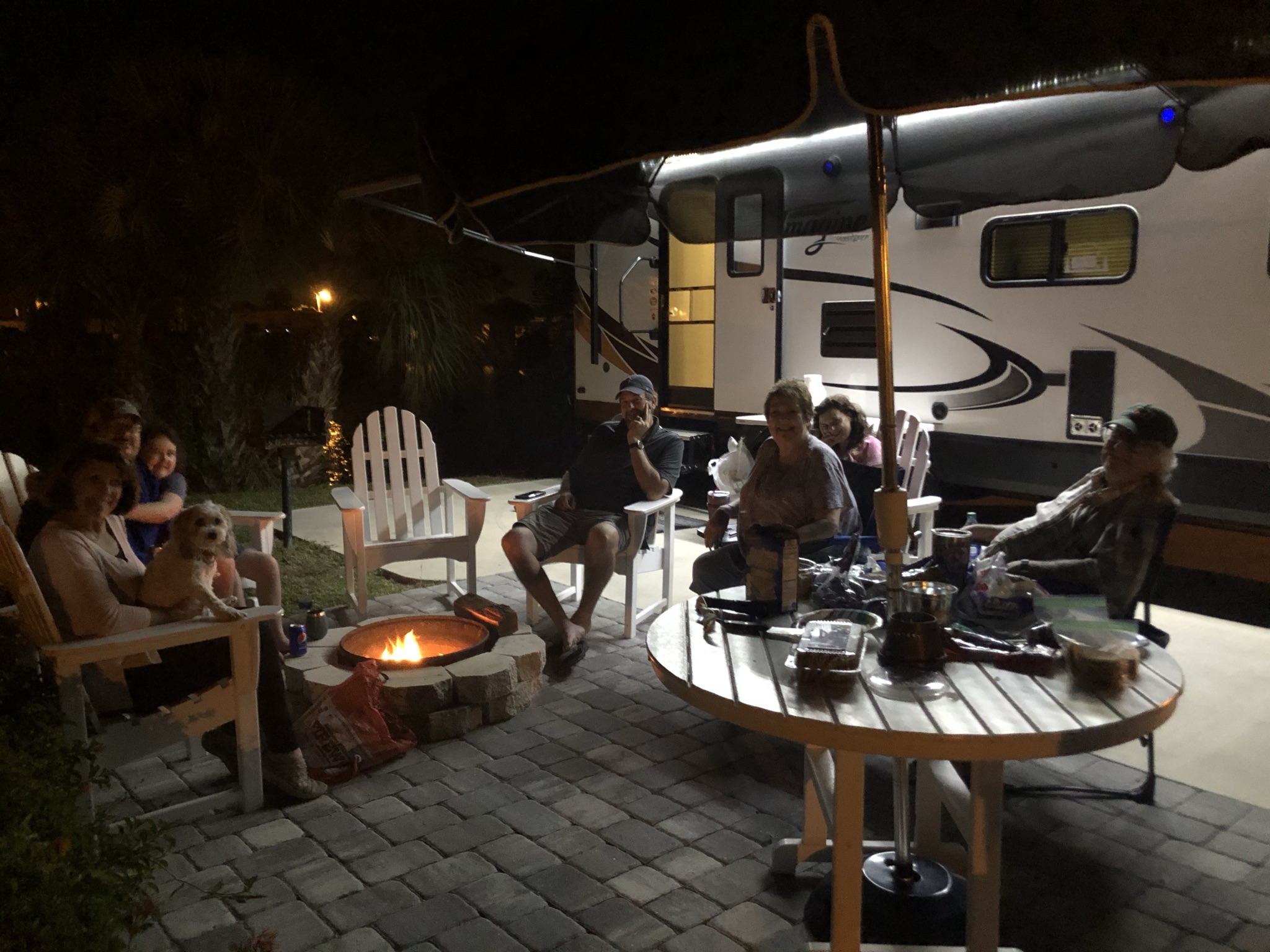 Family relaxing around a fire beside our travel trailer at night